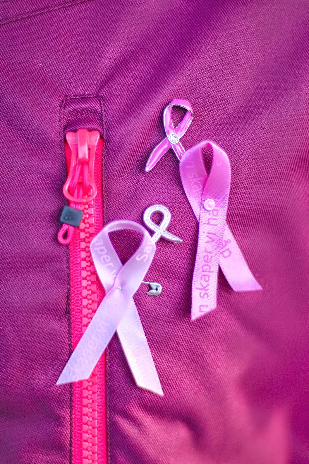 Tre rosa sløyfer festet ved glidelåsen på en rosa vest.