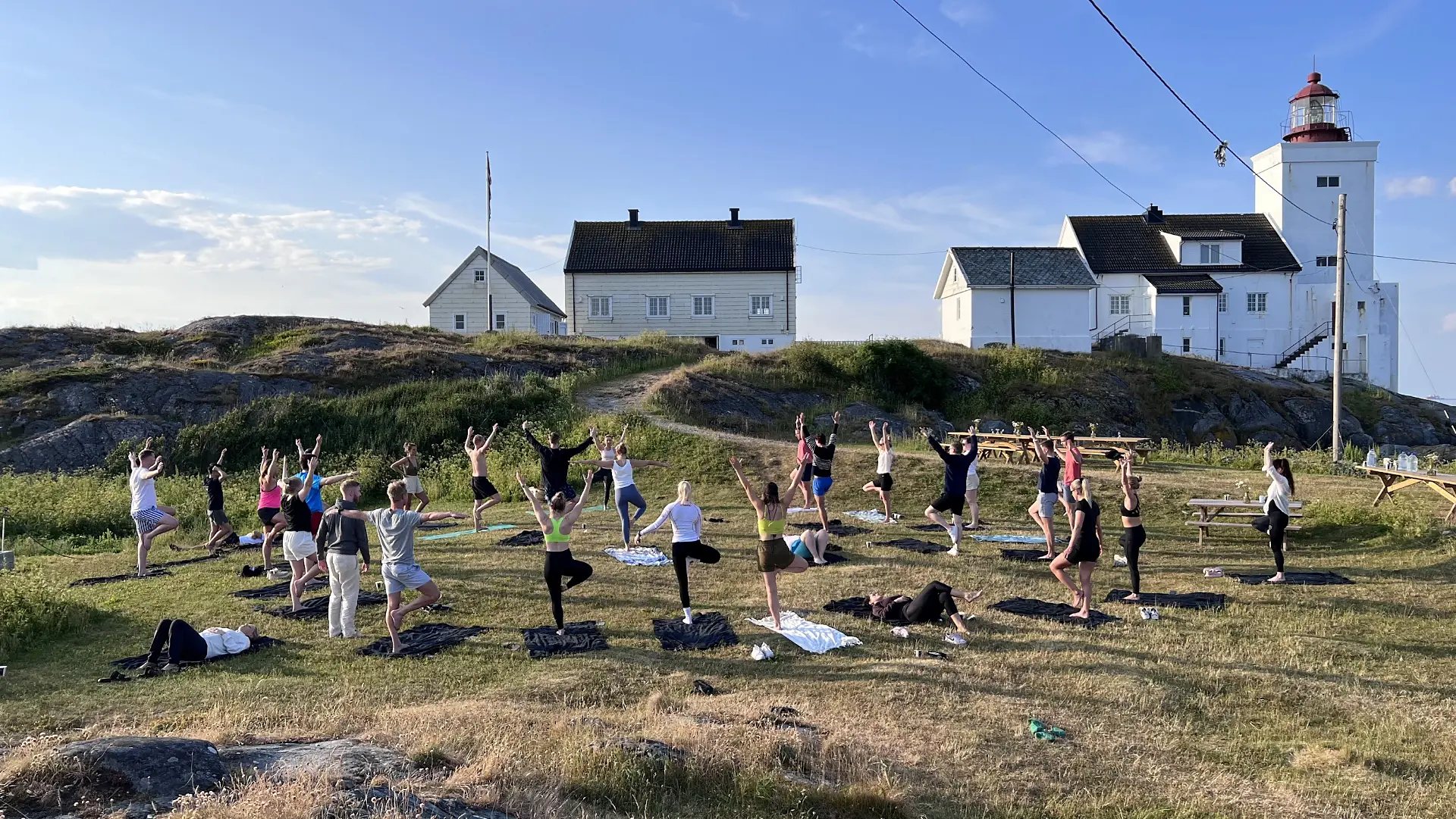 Deltakere gjør yoga på gresset foran fyret og de hvite husene