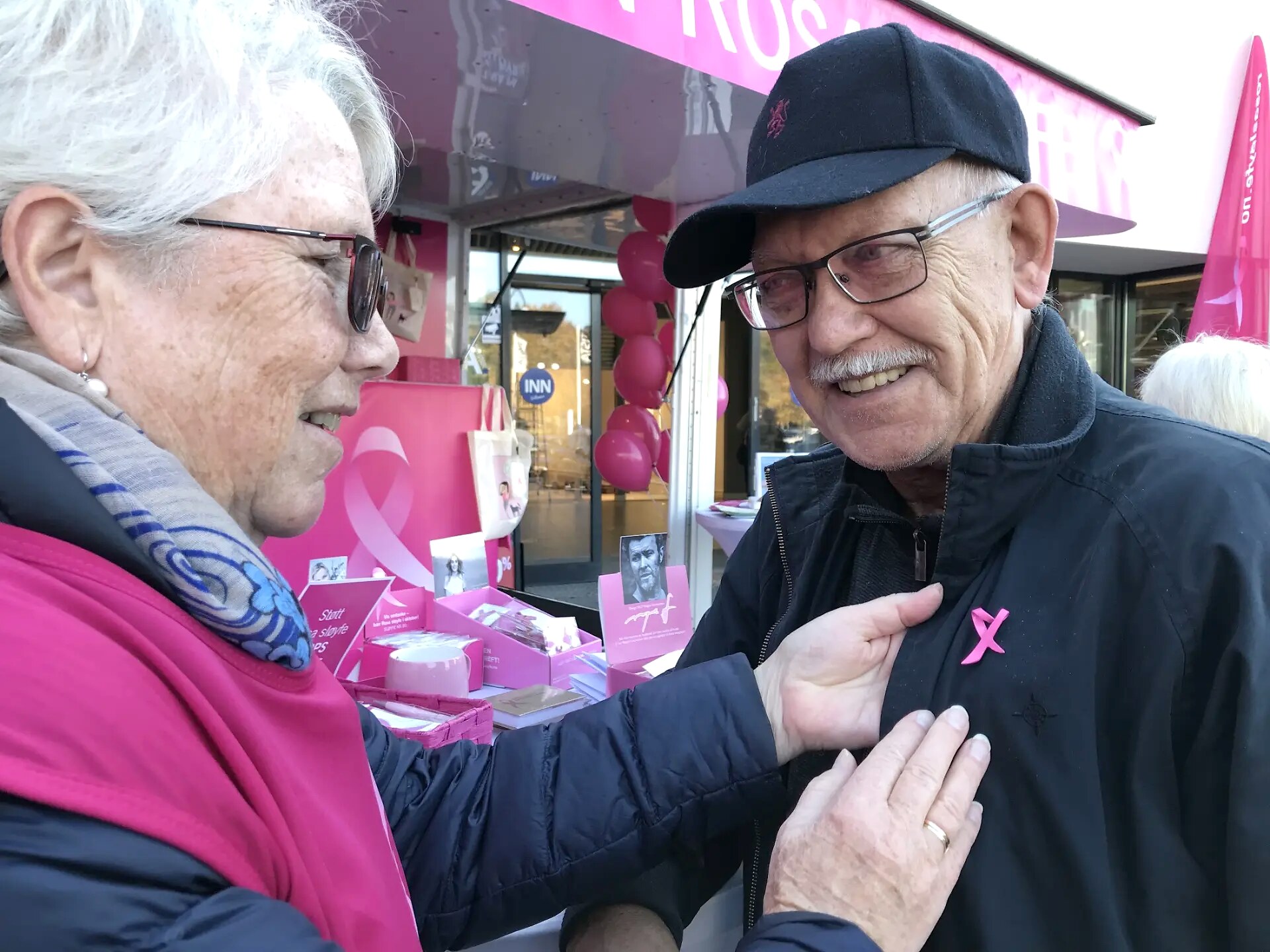 En frivillig fester en rosa sløyfe på jakken til en besøkende ved standen.