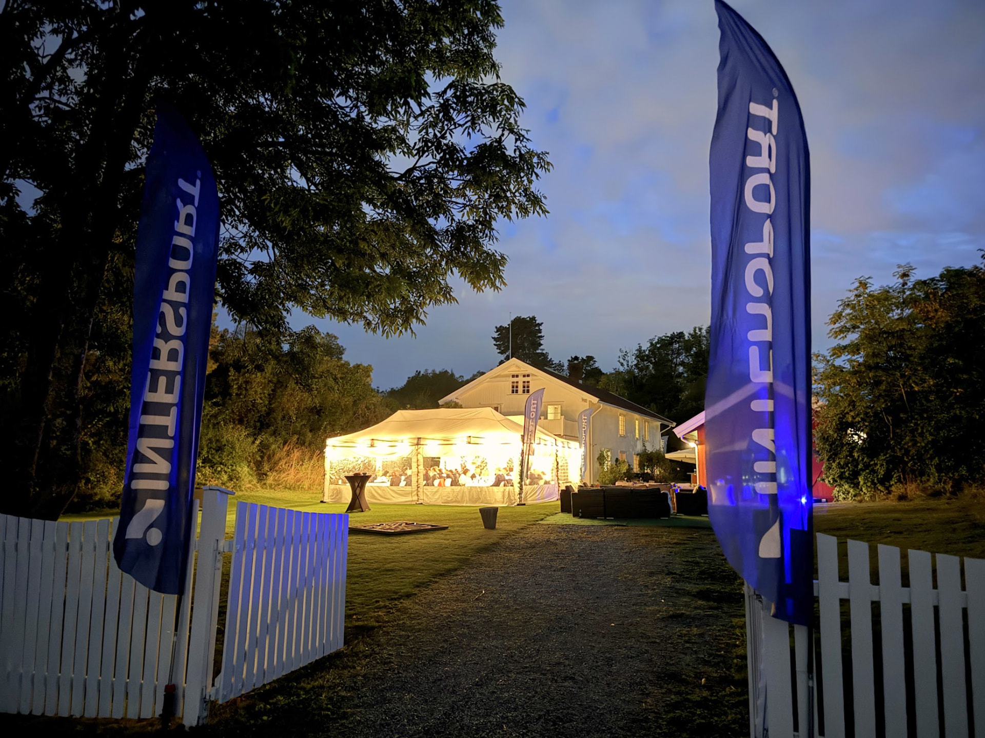 Opplyst middagstelt om kvelden, innrammet av Intersport-flagg.