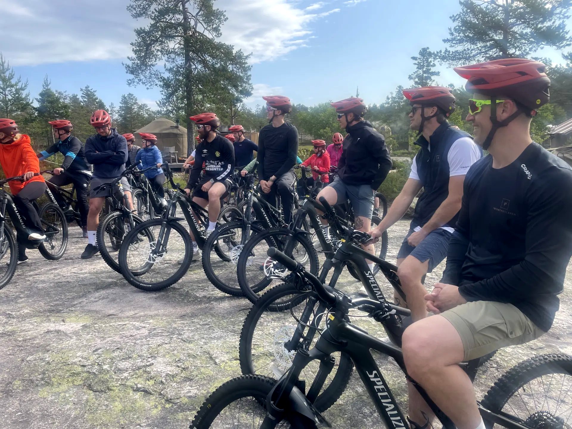 Deltakere med røde hjelmer på sykler, samlet på svaberg