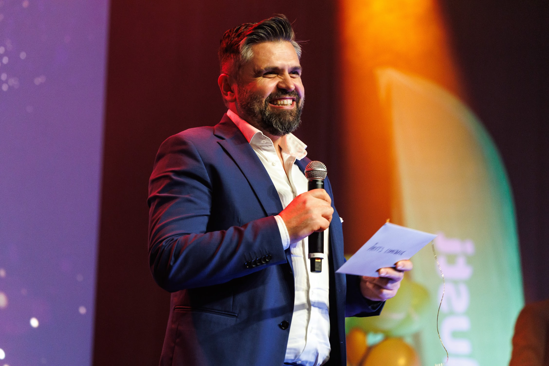 Konferansier med mikrofon og award-kort på scenen i varmt lys