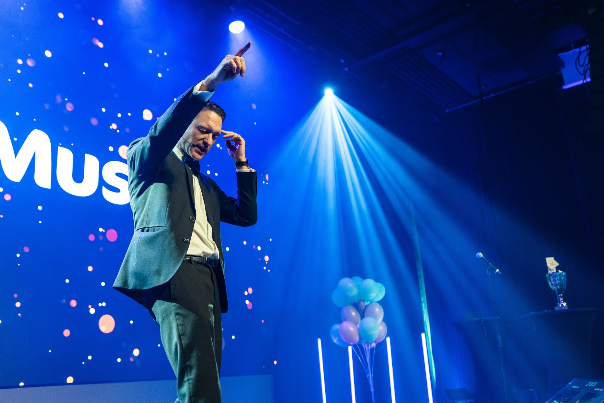 Konferansier på scenen i blått scenelys med ballonger