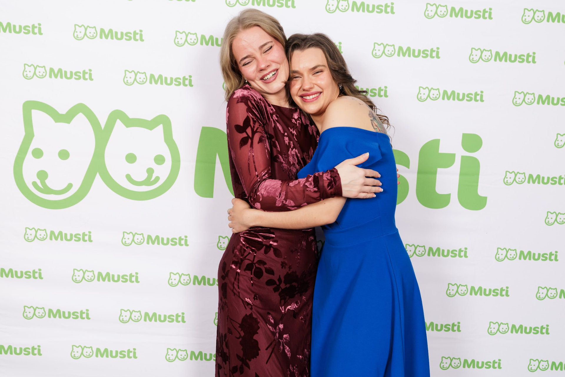To gjester klemmer hverandre foran Musti-fotoveggen under jubileumsfesten