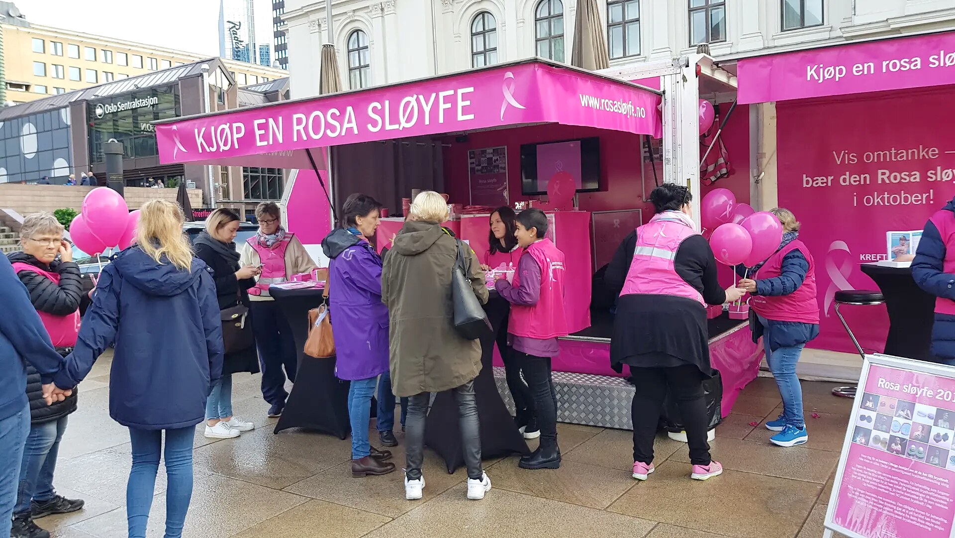 Besøkende og frivillige samlet rundt Rosa sløyfe-hengeren ved Oslo Sentralstasjon.