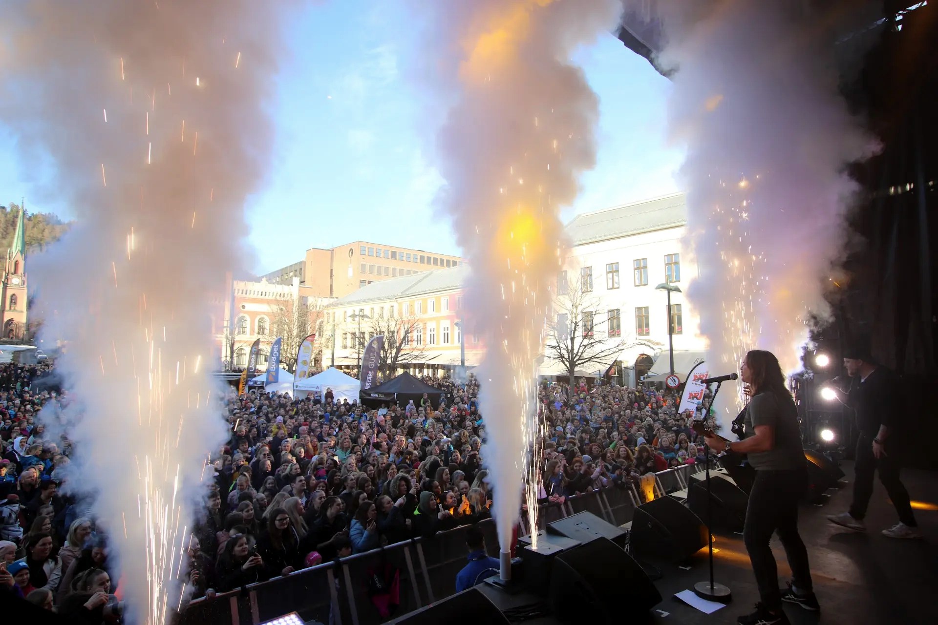 Artist på scenen med pyroteknikk og publikum på bytorget